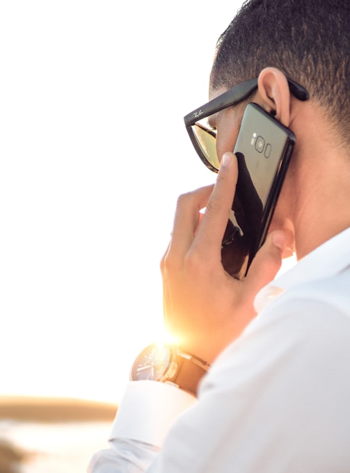 man holding smartphone standing in front of calm body of water